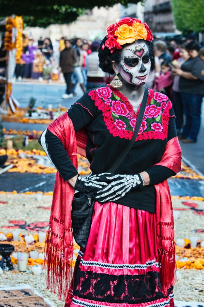 A woman celebrating Día de Los Muertos in traditional garb and face paint